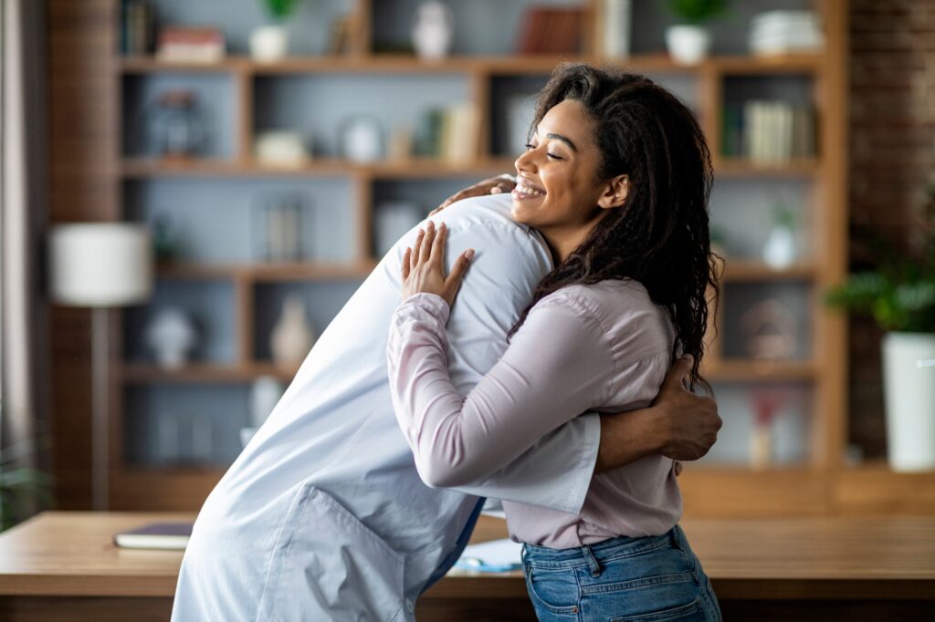 Doctor hugging cheerful black lady patient, clinic interior