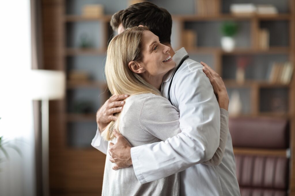 Doctor In Uniform And Female Patient Hugging During Meeting In Office